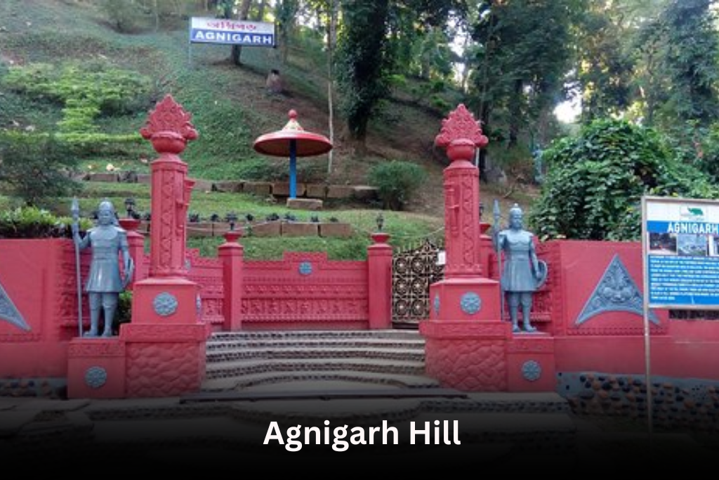 The entrance to Agnigarh Hill in Assam, featuring two statues of warriors on either side of a red gate and stairs leading up a lush, green hill.