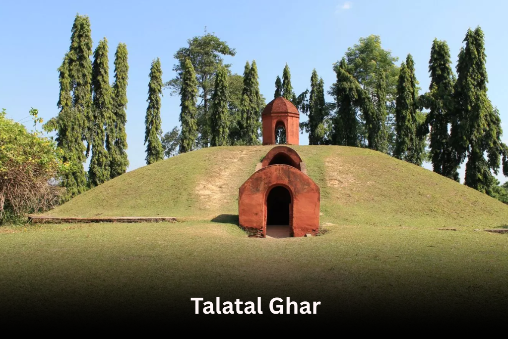 The Talatal Ghar, an ancient Ahom palace, sits atop a grassy mound surrounded by tall, slender trees against a blue sky.
