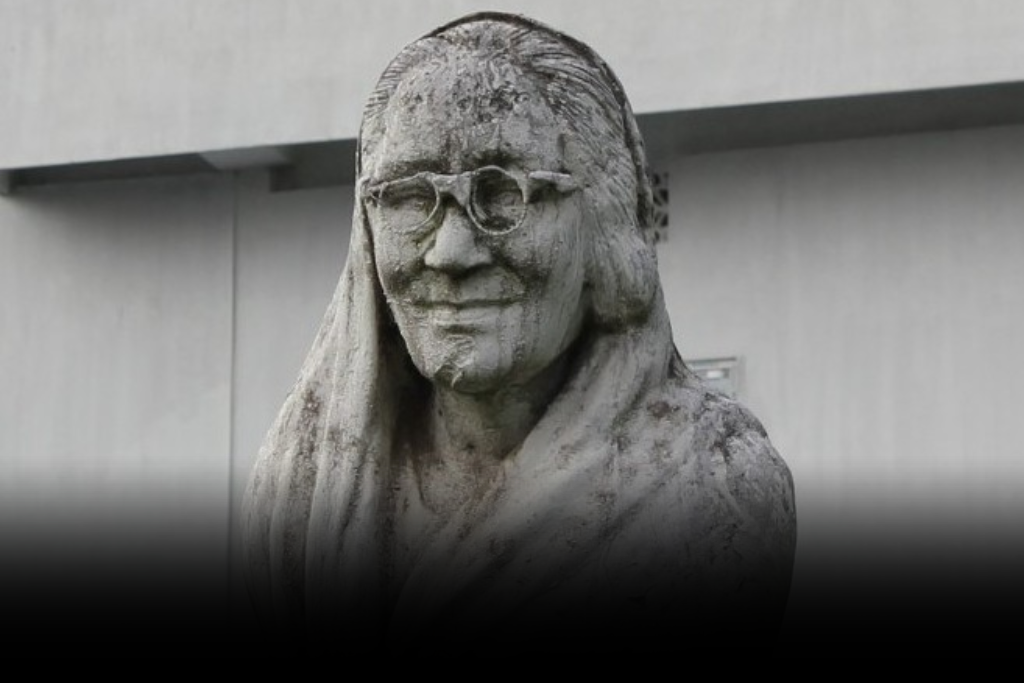 A weathered stone bust of Nalini Bala Devi, an iconic Assamese poet and writer, wearing glasses and a veil.