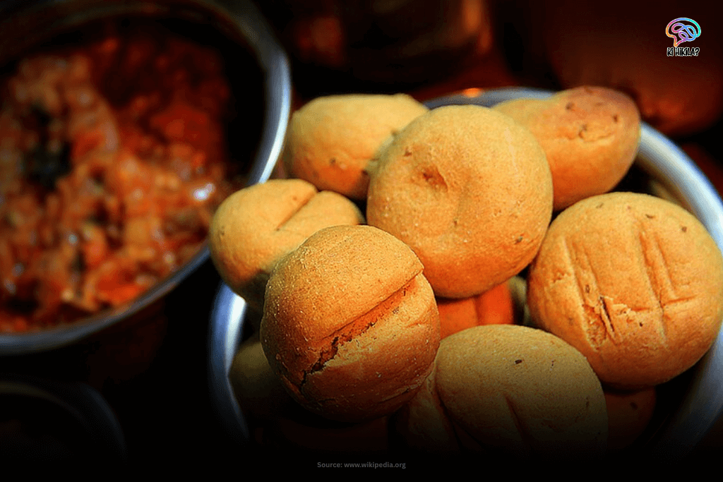 A close-up of Dal Bati Choorma, a traditional Rajasthani dish, featuring several round, baked batis in a bowl next to a serving of dal.