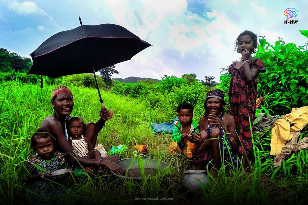 Tribal women and children from the Koraput region of Odisha in a lush green field.