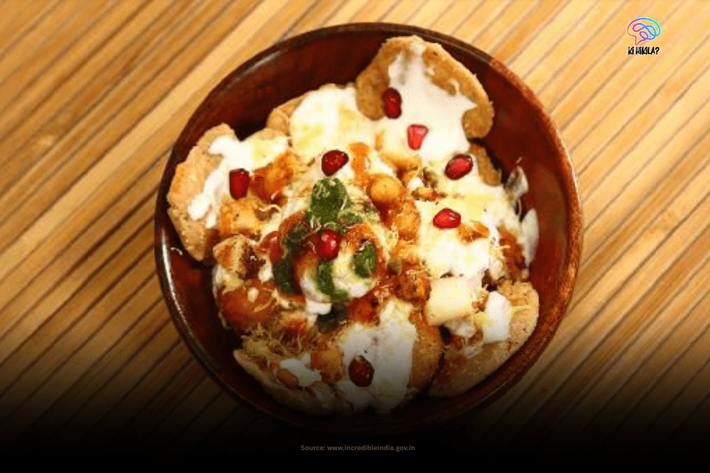 A close-up view of a bowl of Papdi Chaat, a popular street food snack from Delhi, garnished with yogurt and pomegranate seeds.