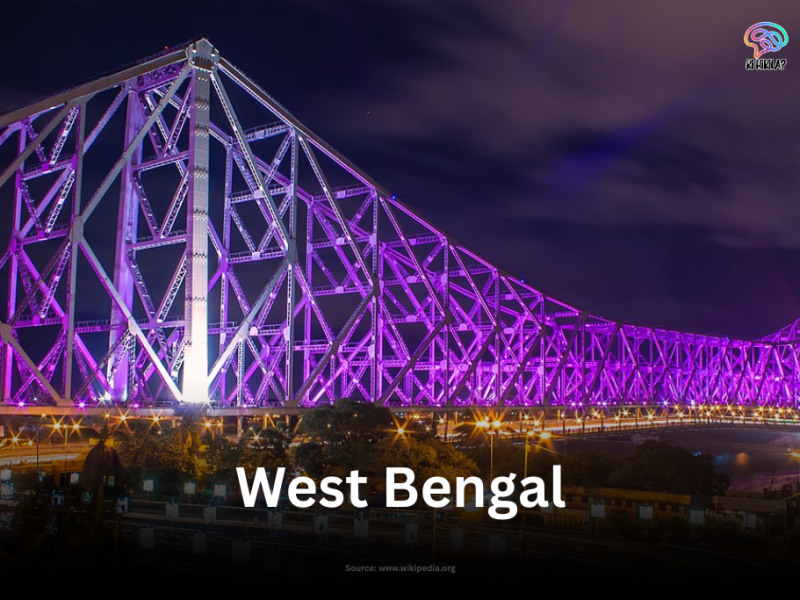 The iconic Howrah Bridge in Kolkata, West Bengal, brilliantly illuminated with purple lights against the dark night sky.