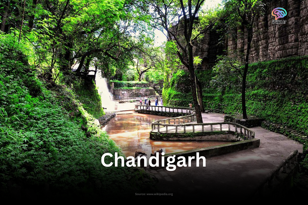 A wide-angle view of the Rock Garden in Chandigarh, showing numerous sculptures made from recycled materials set against a backdrop of artificial waterfalls.