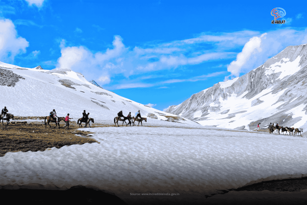 Pilgrims on horseback traverse a snow-covered mountain path in Jammu and Kashmir, with majestic, snow-capped peaks rising in the background.