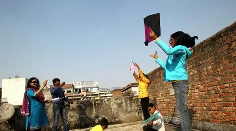 Children and adults flying kites on a rooftop during the Karka Sankranti Festival celebration.