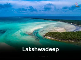 An aerial view of a pristine atoll in Lakshadweep, showcasing the turquoise lagoon, white sandbanks, and lush green coconut groves.