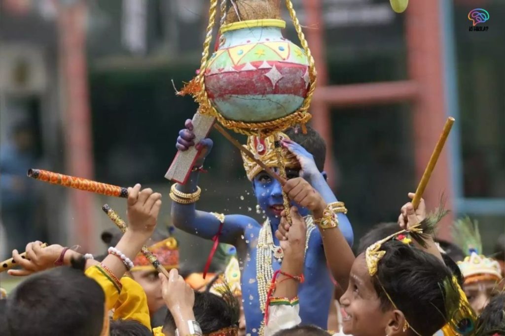 Children celebrating Krishna Janmashtami by breaking the Dahi Handi, dressed as Lord Krishna with painted faces and traditional attire.