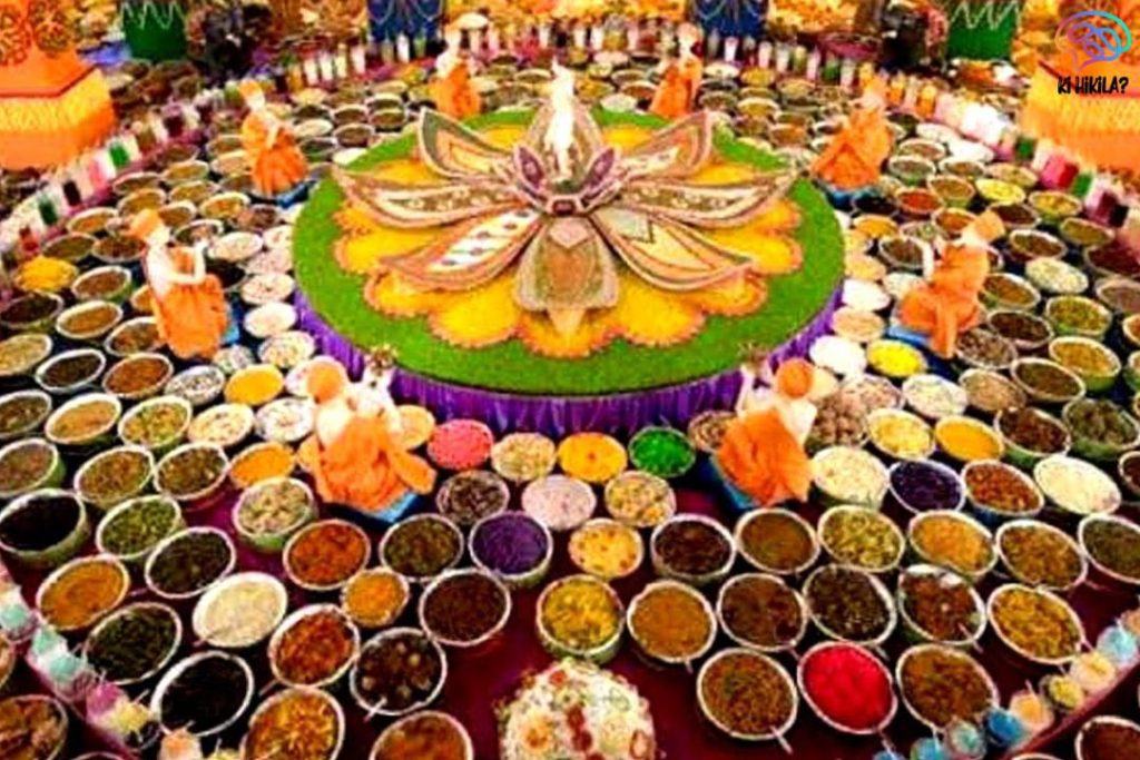A grand Krishna Janmashtami offering with hundreds of colorful dishes arranged in a circular pattern around a floral centerpiece in a temple.