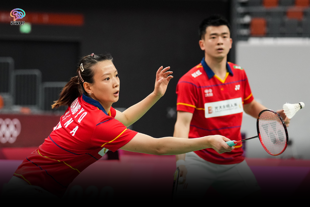 Badminton: An Olympic Sport of Speed, Skill, and Strategy Badminton A female and a male badminton player in red and yellow jerseys on a court, preparing to hit a shuttlecock, representing Badminton in Olympic.